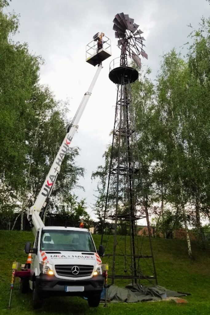 Mit einer Hebebühne sind die Restauratorinnen vor Ort im Gelände und restaurieren ein altes Windrad. Sie sind Experten für technische Restaurierung.